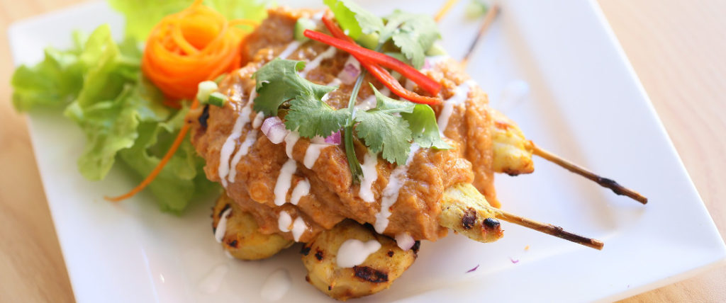 Chicken satay served on a white plate.